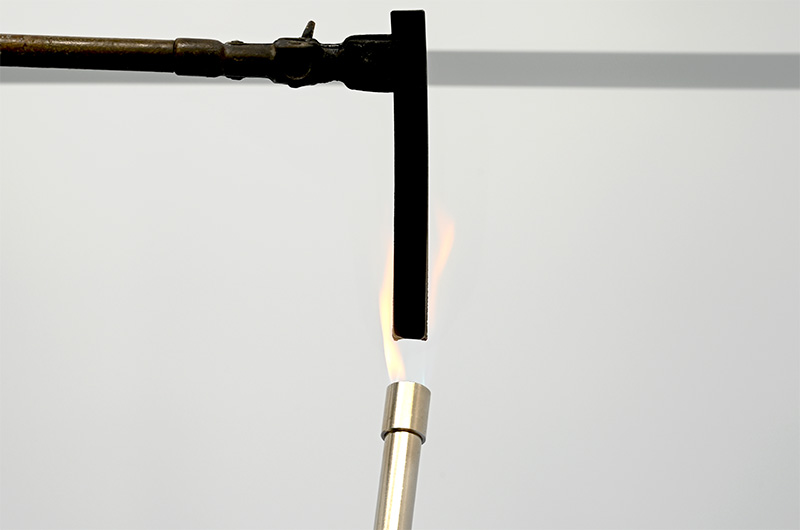 Black ISO-PUR BD50-FR rod is tested using a gas burner according to the UL 94 flame retardancy test.