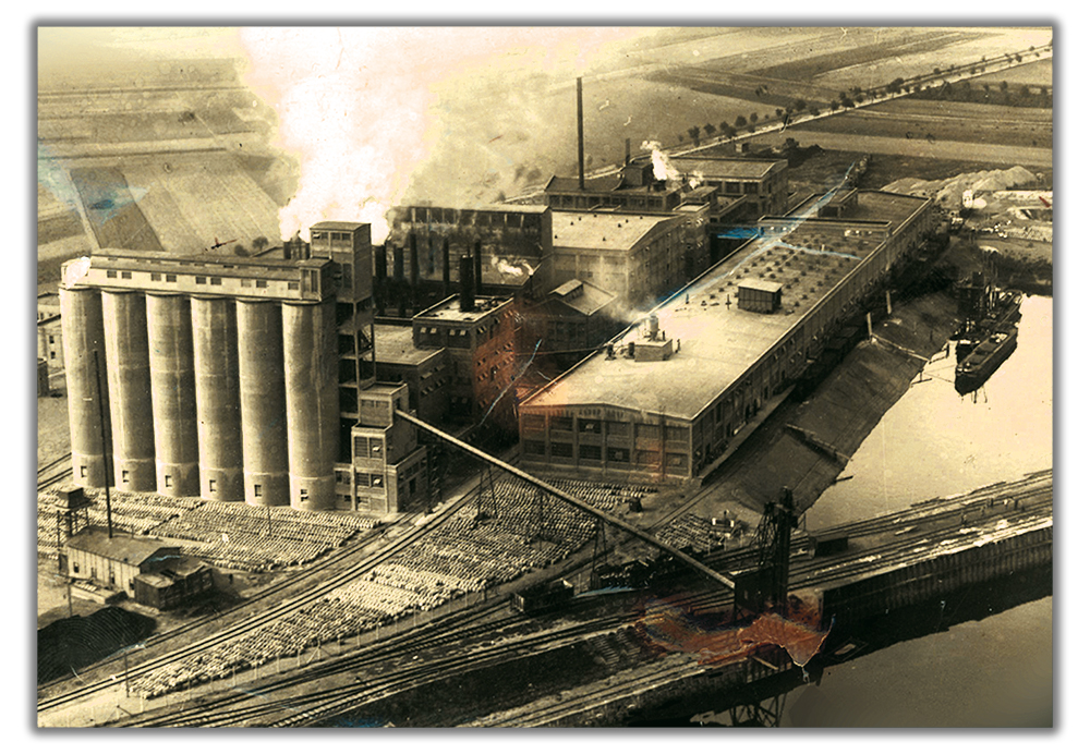 Historische Luftaufnahme des Industriestandorts von Richard Cordes in Elze, gegründet 1906 als Schwesterbetrieb der Carl Cordes AG Magdeburg – Fabrikgebäude mit Silos, Gleisanlagen und Schiffsanlegeplatz am Fluss